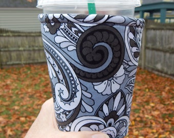 May include: A gray and white paisley patterned cup cozy with a black swirl design.
