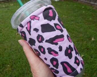 May include: A pink and black leopard print fabric cup cozy for a cold beverage. The cozy is made of a soft, quilted fabric and has a sewn seam around the top edge.