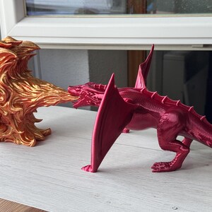 May include: A red dragon figurine with a gold flame figurine blowing fire at it. The dragon has a long tail and wings.