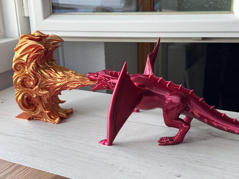May include: A red dragon figurine with a gold flame figurine blowing fire at it. The dragon has a long tail and wings.