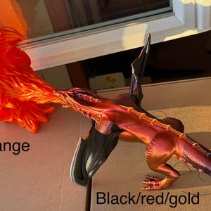 May include: A 3D printed dragon figurine with black, red, and gold paint. The dragon is breathing fire, which is a separate 3D printed piece painted orange.