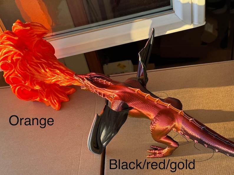 May include: A 3D printed dragon figurine with black, red, and gold paint. The dragon is breathing fire, which is a separate 3D printed piece painted orange.