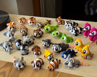May include: A collection of colorful, cartoon animal figurines, including tigers, elephants, penguins, and birds. The figurines are made of plastic and are arranged on a light-colored surface. The animals are in various poses and have large, expressive eyes.