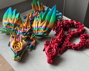 Könnte beinhalten: Zwei 3D-gedruckte Drachenskulpturen, eine mit regenbogenfarbenen Schuppen und die andere mit roten Schuppen. Beide Drachen sind mit Rosen verziert.