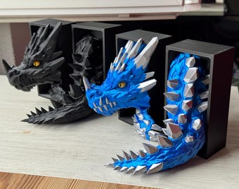 May include: Three dragon bookends. One is black, the other is blue with silver accents. The dragons appear to be emerging from black rectangular boxes. The dragons have yellow eyes and sharp details.