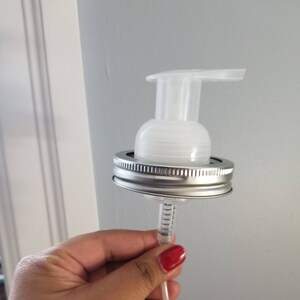 May include: A clear plastic soap dispenser pump with a silver lid and a long clear tube. The pump is attached to a silver lid that fits on a glass jar.