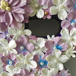 May include: A purple letter R decorated with white and lavender paper flowers. The flowers have pearl accents and some have a light blue center.