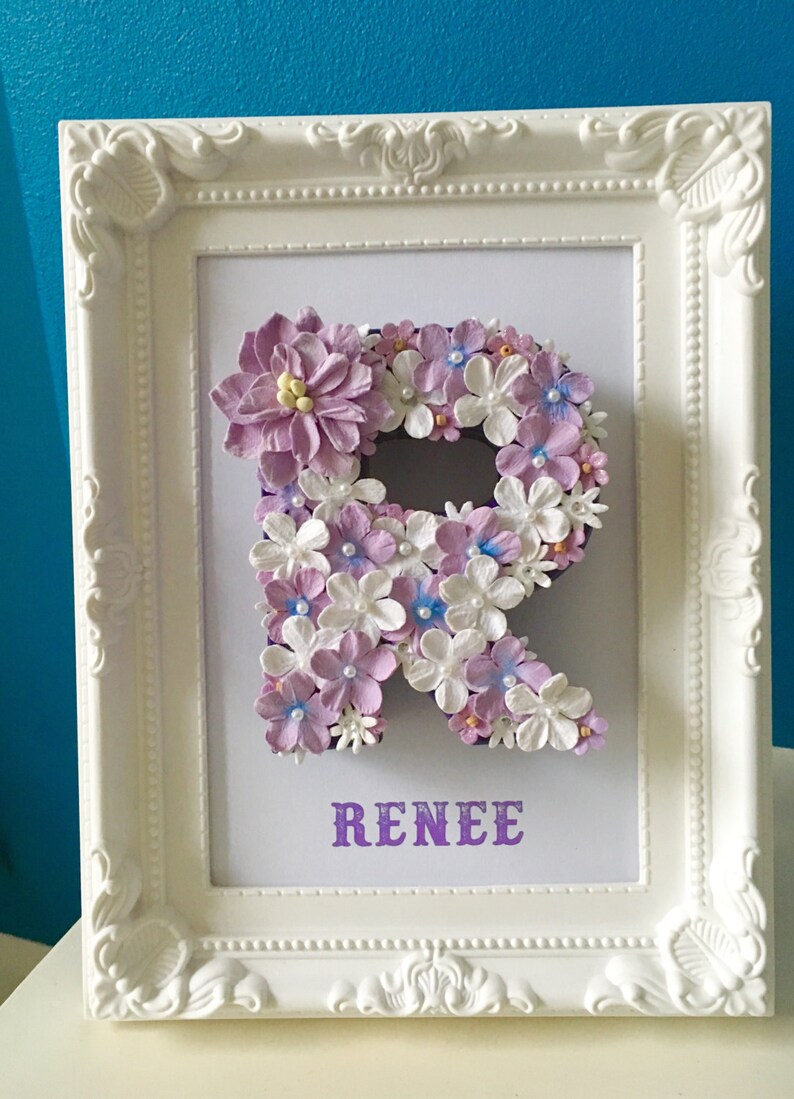 May include: A white frame with a purple letter R made of flowers. The name "RENEE" is written in purple below the letter.