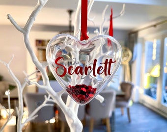 Könnte beinhalten: Ein transparenter herzförmiger Anhänger mit rotem Glitzer im Inneren und dem Namen "Scarlett" in Rot auf der Vorderseite.