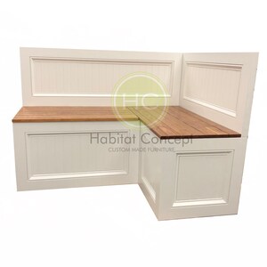 May include: White corner bench with a wood top and a white panel back. The bench has a storage compartment and the text "Habitat Concept Custom Made Furniture" is printed on the front.