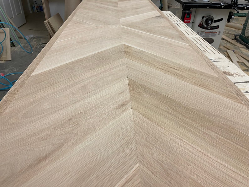 May include: A close-up view of a light wood chevron pattern floor. The wood is a light beige color and the chevron pattern is made up of narrow strips of wood.