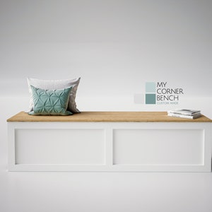 May include: A white bench with a light wood top, featuring two decorative cushions in shades of grey and teal. The bench has a rectangular shape and the text "MY CORNER BENCH CUSTOM MADE" is visible.