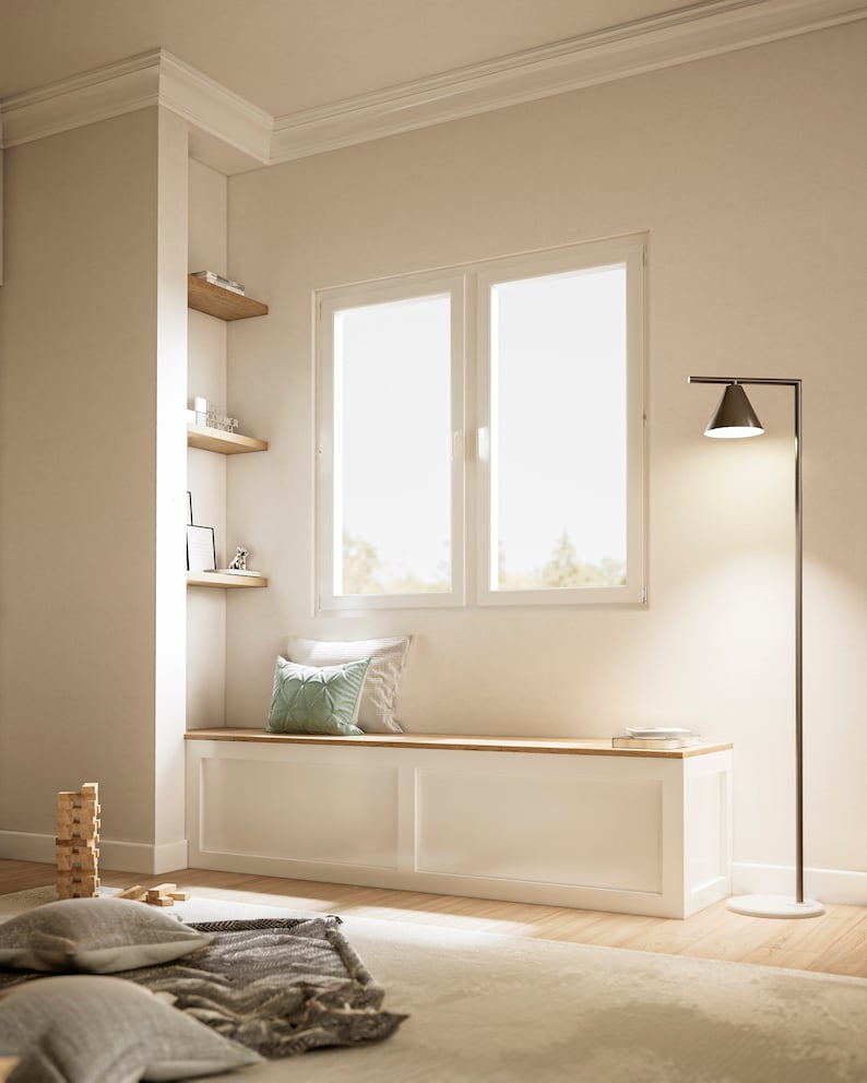 May include: An interior scene with a built-in bench, wooden top, and white paneling. A green cushion sits on the bench, and a modern black floor lamp provides light. A stack of wooden blocks and a rug are in the foreground, creating a cozy atmosphere.