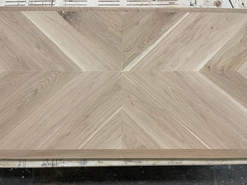 May include: A close-up of a light brown wood floor with a herringbone pattern. The wood is arranged in a geometric pattern with alternating light and dark stripes.