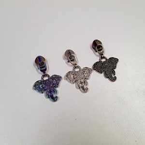 Może przedstawiać: Trzy suwaki do zamków błyskawicznych z motywami słoni. Suwaki są srebrne, czarne i tęczowe.