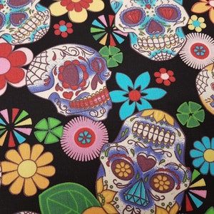 May include: A black fabric with a colorful pattern of sugar skulls and flowers. The skulls are decorated with intricate details and bright colors, including blue, yellow, red, and white. The flowers are also colorful and have a variety of shapes and sizes.