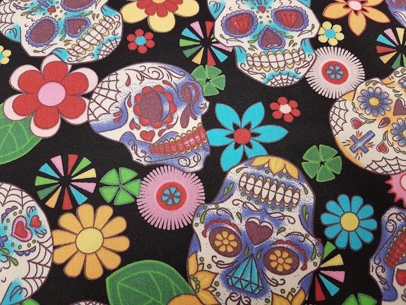 May include: A black fabric with a colorful pattern of sugar skulls and flowers. The skulls are decorated with intricate details and bright colors, including blue, yellow, red, and white. The flowers are also colorful and have a variety of shapes and sizes.