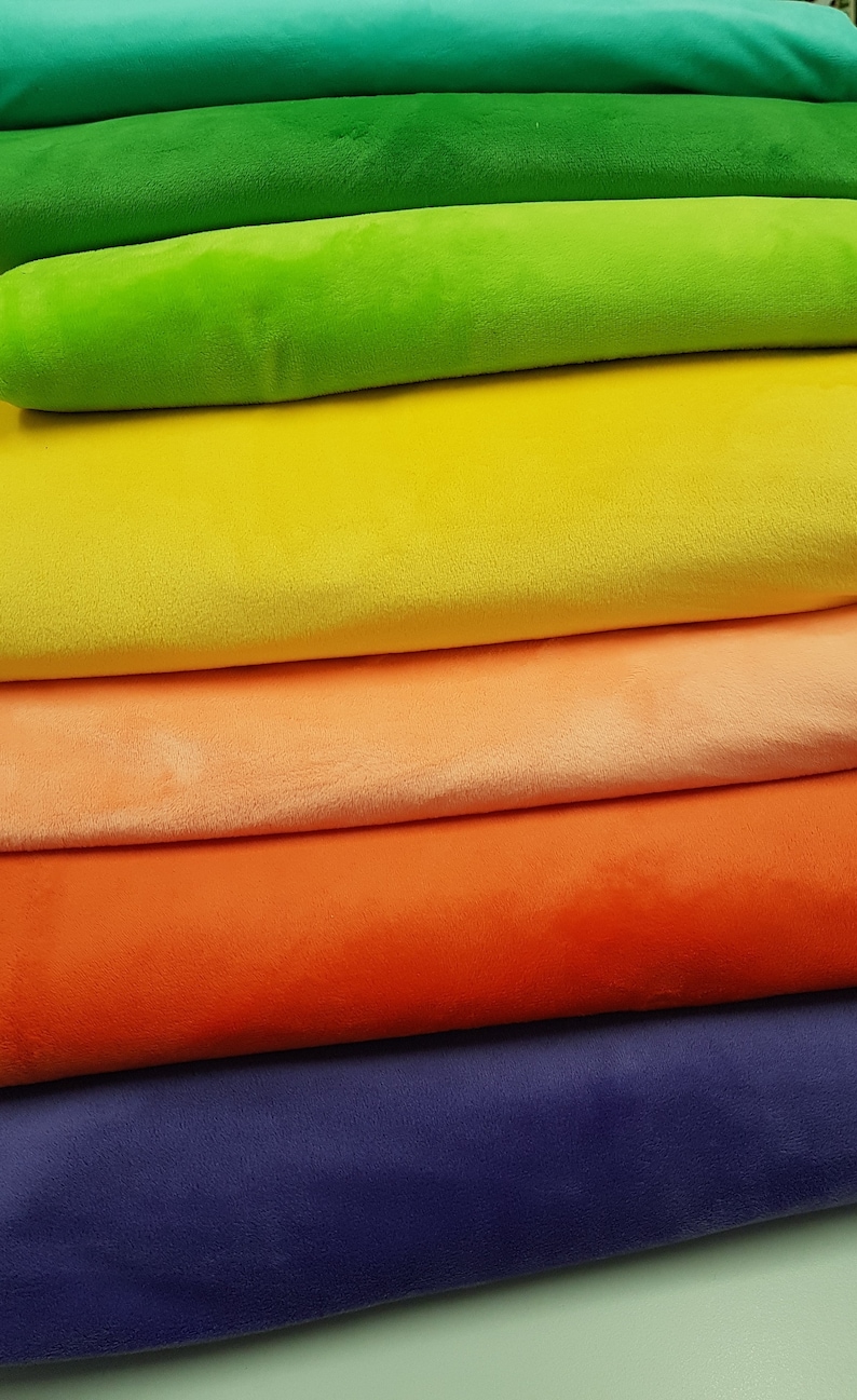May include: A stack of colourful fabric rolls in shades of green, yellow, orange, red, and purple. The fabric is soft and plush, ideal for crafting or sewing projects.