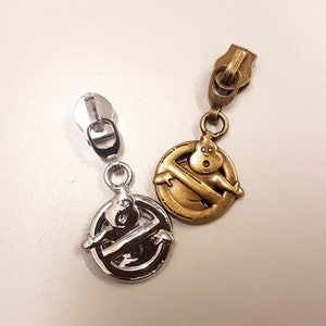 Op de afbeelding: Twee ritsen met een Ghostbusters-logo. Eén is zilver en de andere is goud.