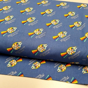 May include: Blue fabric with a repeating pattern of the Millennium Falcon spaceship from Star Wars. The spaceship is yellow, orange, red, and blue with a rainbow behind it. The text "Millennium Falcon" is printed in white below the spaceship.