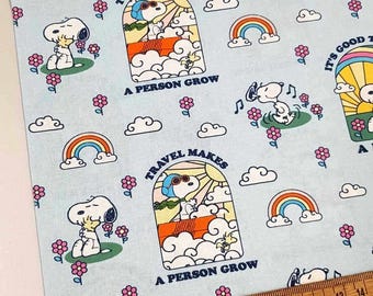 Puede incluir: Tela azul con un patrón repetido de personajes de Snoopy. El patrón incluye a Snoopy volando un avión, Snoopy sosteniendo una flor y Snoopy con Woodstock. El texto "Travel Makes A Person Grow" y "It's Good To Have A Friend" se repite en toda la tela.