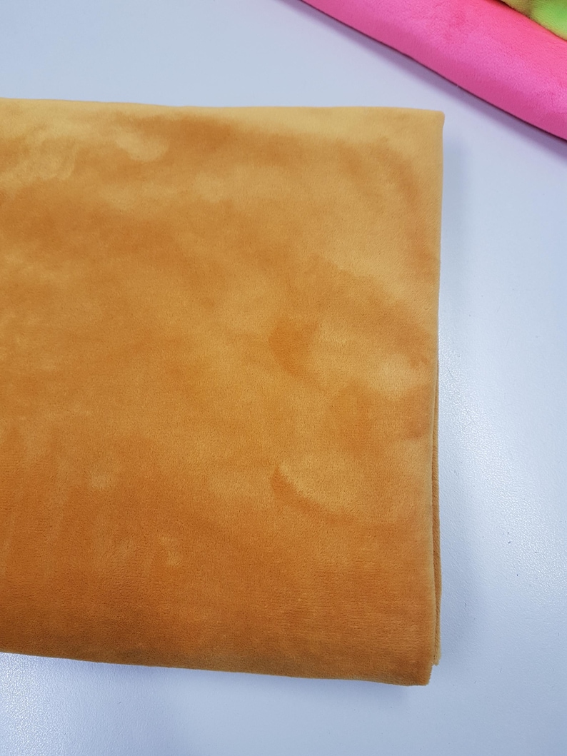 K&ouml;nnte beinhalten: Ein St&uuml;ck weicher, goldgelber Samtstoff. Der Stoff hat einen dezenten Glanz und eine glatte Textur.