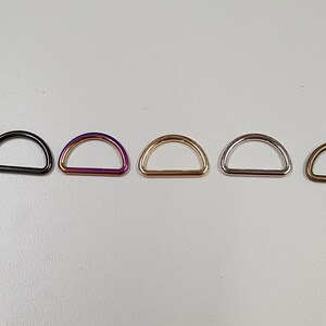 Puede incluir: Cinco anillas en D de diferentes acabados: negro, morado iridiscente, dorado, plateado y bronce.
