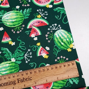 May include: Green fabric with a repeating pattern of watermelons and white flowers. The fabric is measured with a wooden ruler.