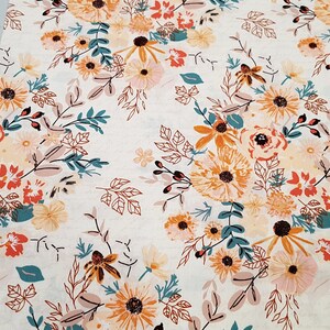 May include: A white fabric with a floral pattern featuring orange, yellow, pink, and teal flowers. The background is a light cream color.