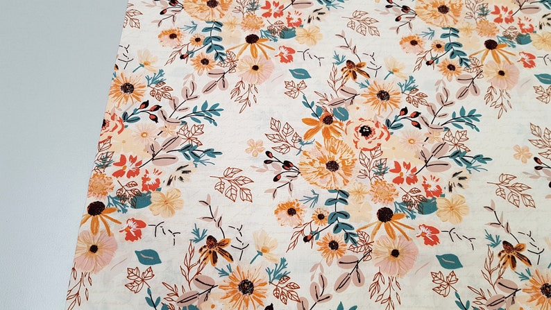 May include: A white fabric with a floral pattern featuring orange, yellow, pink, and teal flowers. The background is a light cream color.
