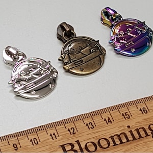 May include: Three zipper pulls featuring a cartoon character. The zipper pulls are silver, bronze, and iridescent.