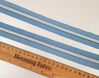 May include: Two pieces of light blue zipper tape with a white zipper coil. A wooden ruler with the text "Blooming Fabric" is in the bottom of the image.