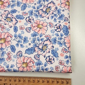 Könnte beinhalten: Weißer Stoff mit einem rosa-blauen Blumenmuster. Der Stoff wird mit einem Lineal gemessen, das Zoll anzeigt.