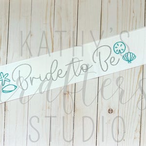May include: White satin sash with the text "Bride to Be" in teal lettering. The sash is decorated with teal seashells and a starfish.