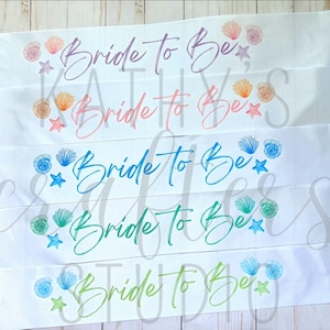 May include: White satin sashes with the text "Bride To Be" in various colors. Each sash is decorated with watercolor seashells and starfish. The sashes are perfect for a bridal shower or bachelorette party.