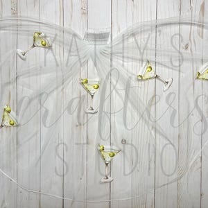 May include: White tulle veil with a pattern of martini glasses with olives. The veil is tied with a white ribbon.