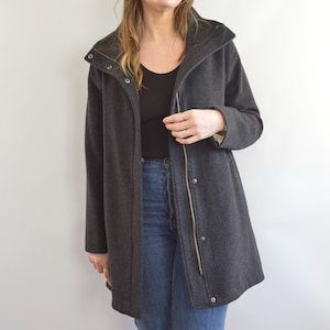 May include: A dark gray coat with a high collar and a zipper closure. The coat has a long length and a tailored fit. The coat is made of a soft, wool-like material. The coat has a button closure and a small pocket on the front.