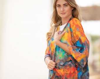 Pode incluir: Uma mulher vestindo um quimono de estampa abstrata colorida com mangas compridas e fecho de nó. O quimono tem tons de laranja, amarelo, azul e verde.