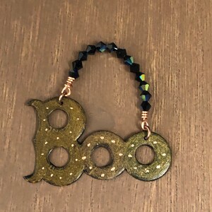 May include: A green wooden "BOO" ornament with gold polka dots and a black beaded hanger.