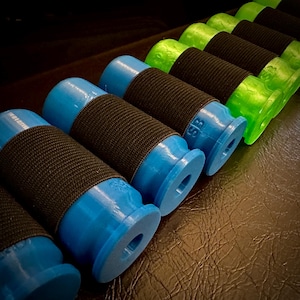 Puede incluir: Una fila de objetos cilíndricos azules y verdes con bandas elásticas negras envueltas alrededor de ellos. Los objetos están dispuestos en un patrón escalonado, con los objetos azules en primer plano y los objetos verdes en el fondo.