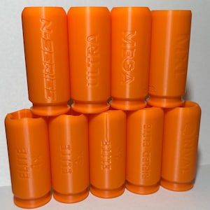 Puede incluir: Una colección de diez accesorios de plástico de color naranja brillante. Los accesorios cilíndricos presentan texto en relieve, incluyendo "N-SERIES", "ULTRA", "MEGA", "RIVAL" y "ELITE". Los artículos están dispuestos en dos filas, mostrando sus variados diseños.