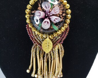 Colgante: cabujón de flor de cristal, detalle de pan de oro, rocallas, borlas y cadena de oro