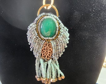 Colgante: Calcedonia verde, cabujón, rocallas de jade, acento dorado, borlas