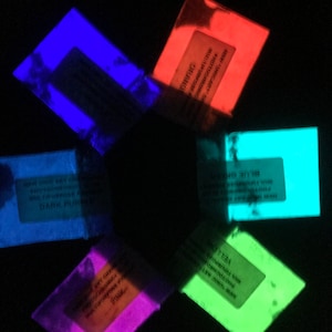 May include: Six small packets of glow-in-the-dark powder in different colors: blue, orange, dark purple, pink, green, and light blue. The packets are labeled with the color and the words "Photochromic Glow in the Dark Pigment".