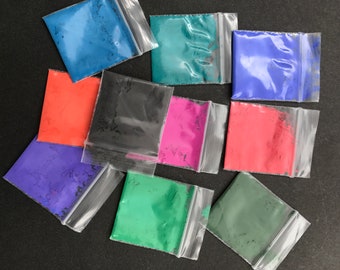 May include: Assortment of small plastic bags filled with colorful powder pigments. The colors include blue, red, green, black, and purple.