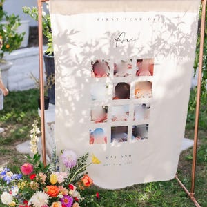 Könnte beinhalten: Ein weißes Canvas-Banner mit einem Kupferrahmen, das eine Fotocollage des ersten Lebensjahres eines Babys zeigt. Das Banner lautet "First Year of Ari" und "Oct 5th, 2022".