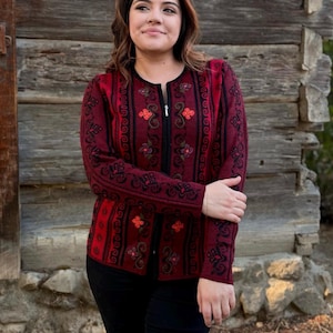 May include: A burgundy cardigan with black embroidered floral patterns and a zipper closure.