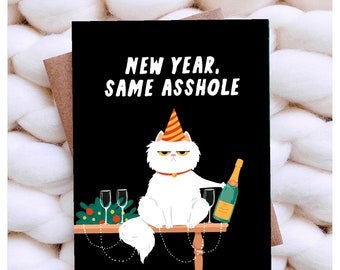 May include: A greeting card with a black background features a white cat wearing a party hat and holding a champagne bottle. The text reads "NEW YEAR, SAME ASSHOLE". Two champagne glasses and festive decorations are on the table.