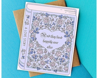 Pode incluir: Um cartão azul claro com um design floral e o texto "And they lived happily ever after" em forma de coração. O cartão tem a forma de um livro e diz "A Love Story" no lado.