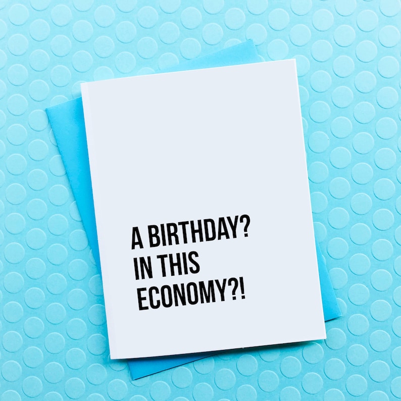 May include: A white card with black text that reads "A birthday? In this economy?!" The card is on a blue background with a pattern of small circles.